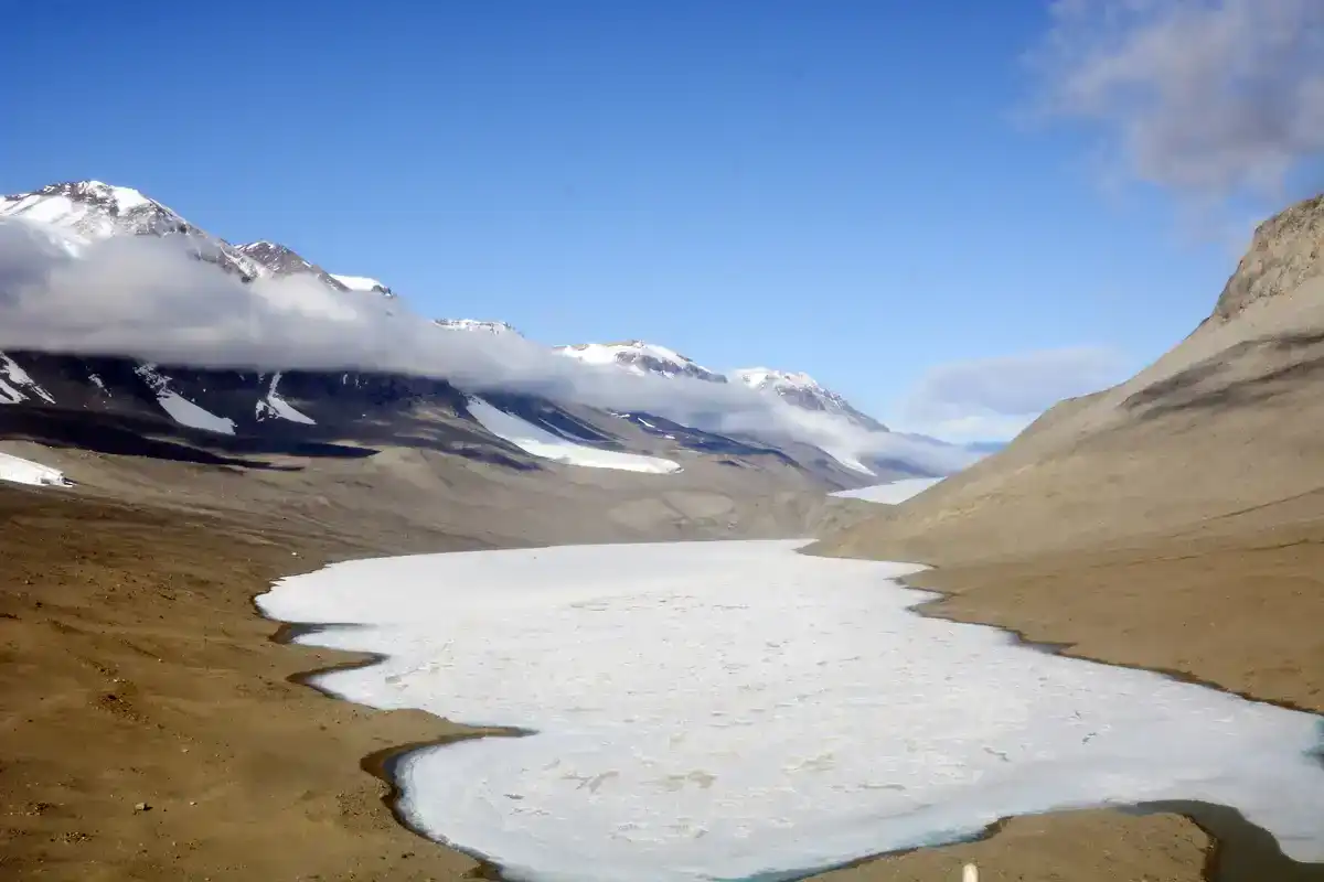 Ice-covered Lake Bonney surrounded by bare brown slopes and snowy peaks in the McMurdo Dry Valleys of Antarctica