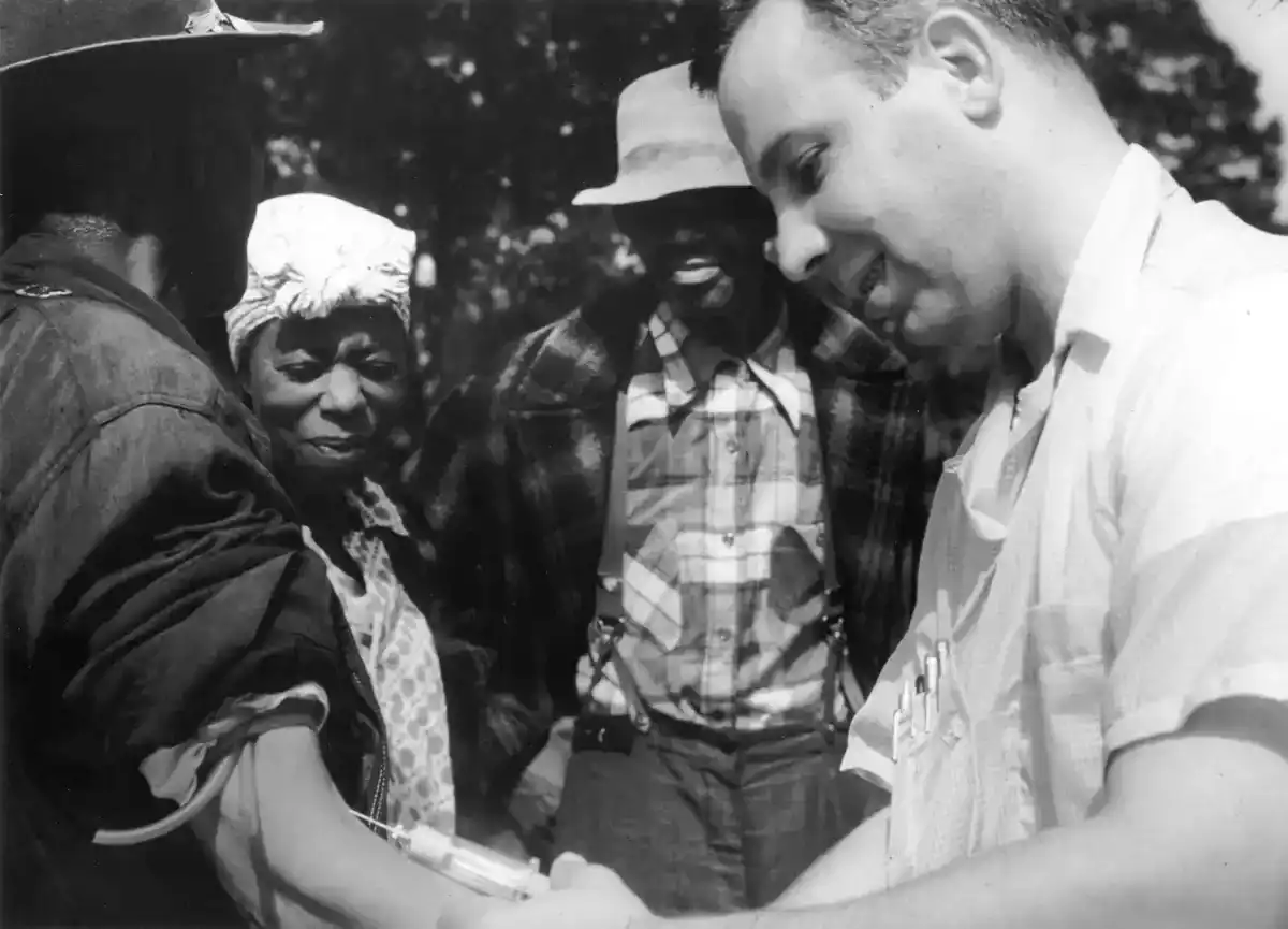 Doctor draws blood from a participant's arm during the Tuskegee syphilis study as other participants look on