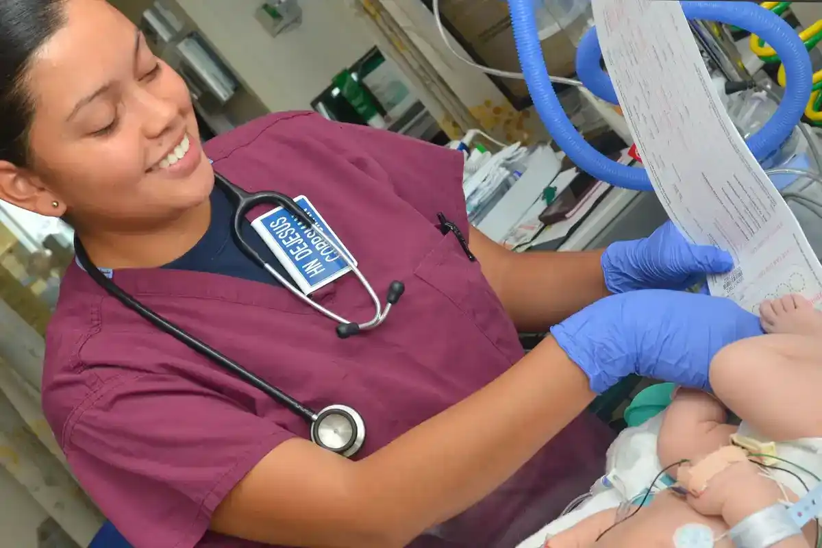 Navy hospital corpsman holds a newborn screening blood spot card next to a baby's foot in a hospital unit