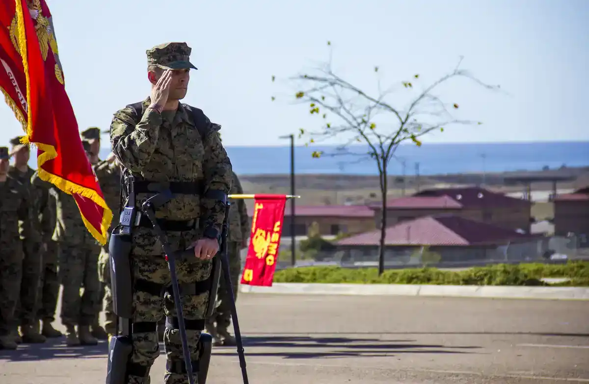 Marine officer paralyzed in combat salutes while standing in a powered exoskeleton with forearm crutches