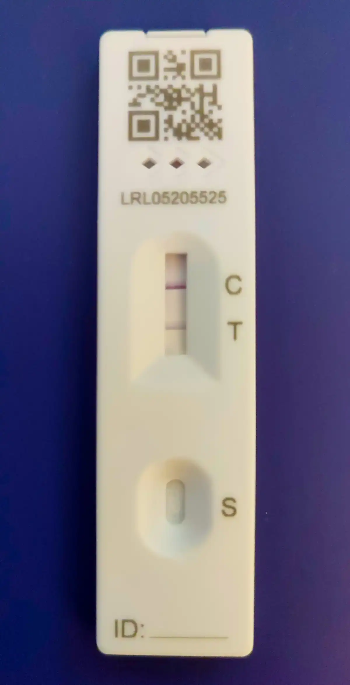 Lateral flow antigen test cassette showing a positive result. Two coloured lines are visible in the result window, one at the control position marked C and a second at the test position marked T, with the sample well marked S below.